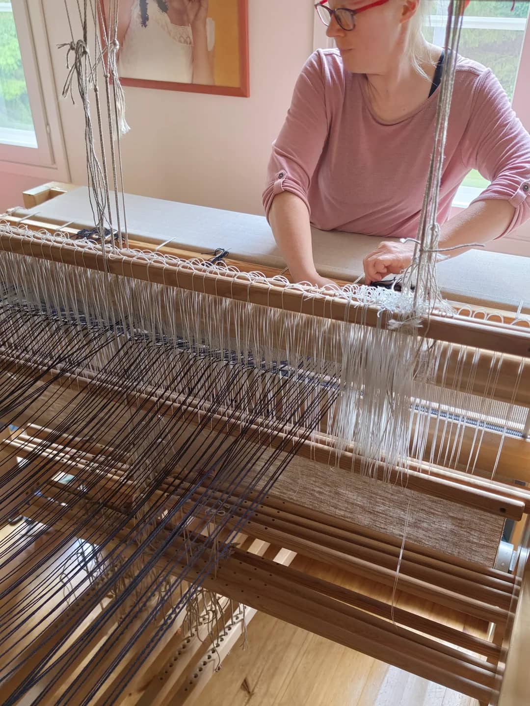 Hands warping a wooden loom with tensioned threads.