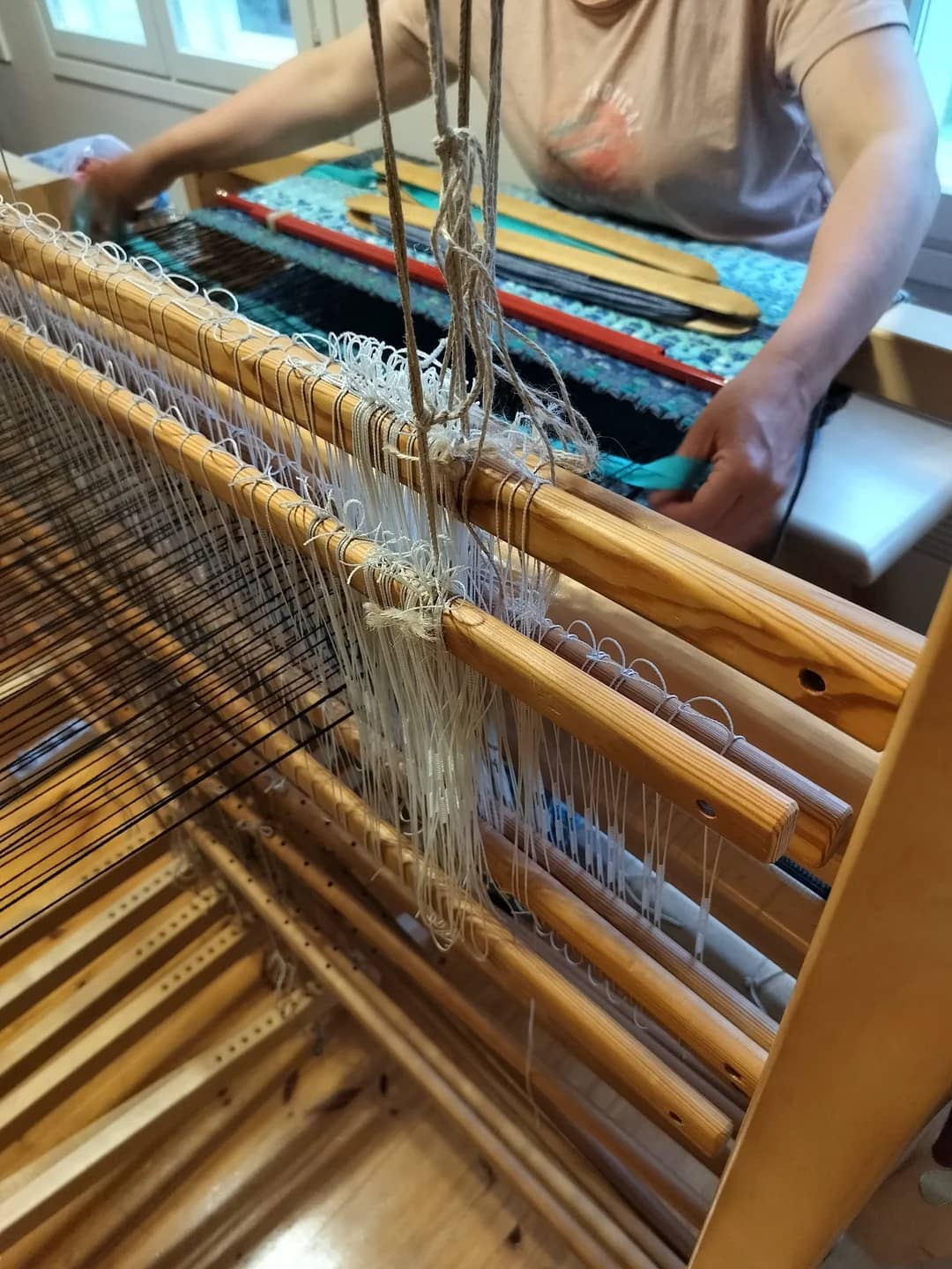 Weft threads passing through warp on a wooden loom.